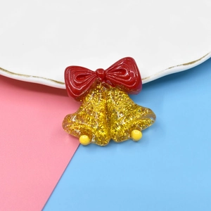 Macro shot of glitter resin gold Christmas bells with a red bow on a white plate