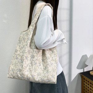 Floral canvas tote bag with blue patterns shown on model's shoulder in natural light