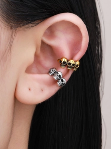 Close-up of punk style skull ear cuffs in gold and silver finish worn on the ear bone
