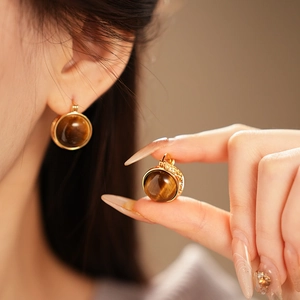 Vue détaillée de boucles d'oreilles dorées avec pierre œil de tigre et gravures