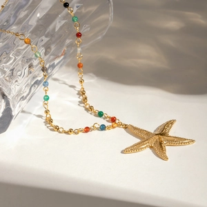 Detail of bohemian gold starfish necklace with colorful beads on glass bottle