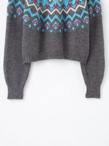 Close-up of Fair Isle geometric jacquard pattern on dark grey knit sweater with ribbed cuffs