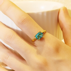 Detail of 18K gold plated ring with square blue gemstone worn on finger