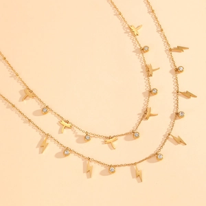 Détail d'un collier doré double épaisseur avec pendentifs libellule, éclair et zircons