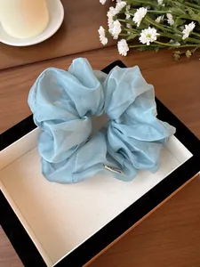 Dettaglio di scrunchie in organza azzurro con pieghe morbide ed etichetta in scatola regalo