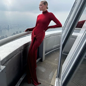 Détail d'une robe rouge à col montant et manches longues avec nœud à la taille et jupe longue