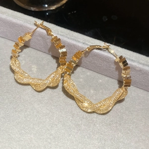 Macro shot of gold twisted rope hoop earrings with square metal details on gray velvet