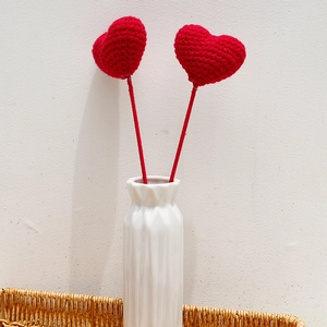 Close-up of two red crochet hearts in a white ceramic vase with a clean beige background