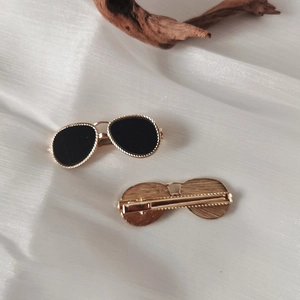 Close-up of golden sunglasses-shaped hair clips with black lenses on white silk background