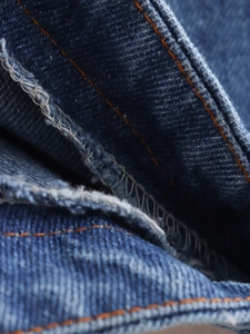 Close-up of blue denim fabric showing orange contrast stitching and overlock seam finish