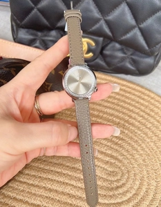 Detailed view of women's watch with crystal-set silver dial and grey leather strap worn on wrist