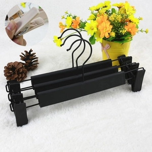 Close-up of adjustable non-slip black plastic pants hangers with sliding clips on soft carpet