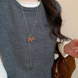 Macro detail of gold Y-shaped necklace with sliding brown terrier puppy pendant on grey sweater