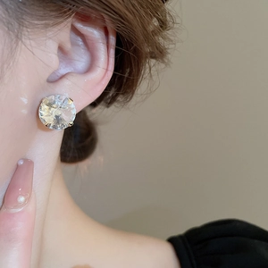 Close-up of a model wearing large round crystal stud earrings in silver finish