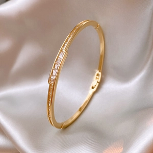 Makroaufnahme des vergoldeten Armbands mit Zirkonia-Steinen auf champagnerfarbener Seide