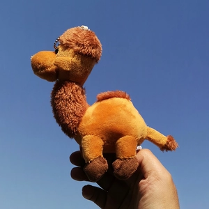 A detailed close-up shot of a soft camel plush keychain held up against a clear blue sky