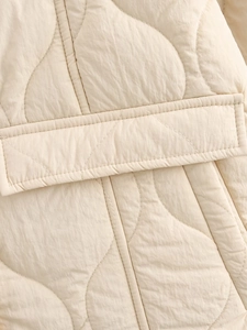 Detailed view of beige quilted cotton coat featuring wavy stitching and a pocket flap