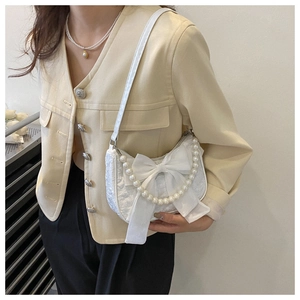 Detail of white lace shoulder bag with large velvet bow and elegant pearl chain strap