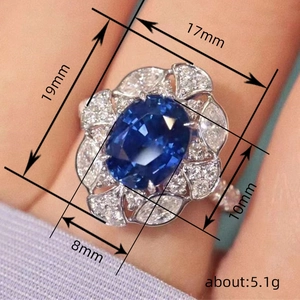 Royal blue sapphire ring with sparkling floral halo and silver tone band worn on hand
