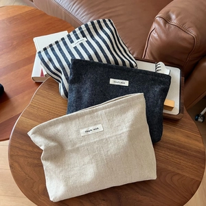 Three minimalist fabric cosmetic pouches in striped and solid textures on a wooden table