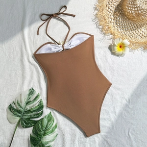 Flat lay of brown halter one-piece swimsuit with white trim and tropical vacation decor