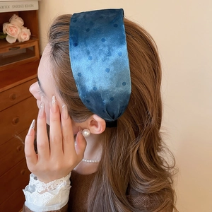 Close-up of navy velvet wide headband with flocked polka dots on a model wearing pearls
