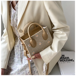 Detail shot of a beige straw woven mini bag with white daisy embroidery and crossbody strap