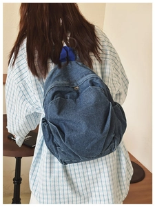 Rear view of a model wearing the dark blue denim backpack with a top handle and zippers