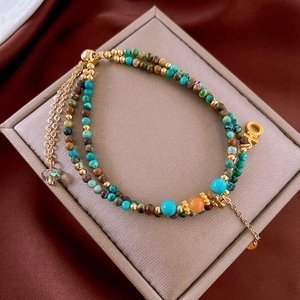 Dettaglio del bracciale a doppio strato con pietre turchesi e ciondoli dorati lucidi