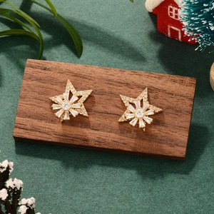 Close-up of gold star earrings with clear gems on wooden block with Christmas decor