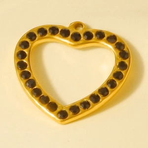 Detail of gold heart pendant with black rhinestones on a minimalist beige background