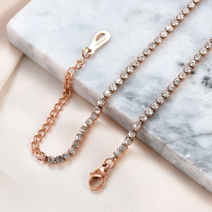 Elegante rotgoldene 3mm Tenniskette mit klaren Kristallen auf Marmor und Seide