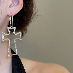 Detailed view of large silver cross hollow earrings with metallic texture worn on ear