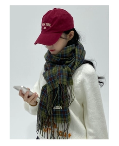 Detail shot of green plaid scarf with fringes styled with a red New York baseball cap
