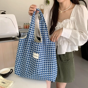 Stylish blue and white checkered woven tote bag worn by a model in a cafe setting