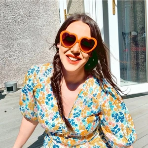 Close-up of orange heart-shaped sunglasses with gradient lenses on a female model