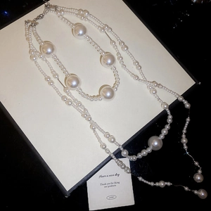 Detailed view of layered faux pearl necklace with silver chains on a jewelry box