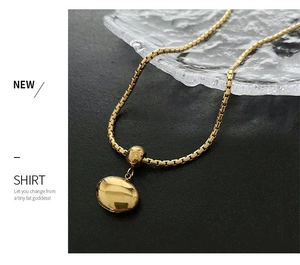 Close-up of golden box chain necklace with high-polished pebble pendant on black texture