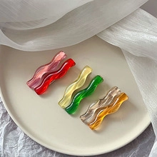 Detailed close-up of six wavy acrylic hair clips in assorted colors on a beige plate