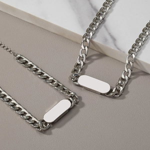 Silver Cuban chain necklace and bracelet set with rectangular tags on marble surface