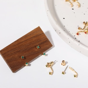 Detailed close-up of gold stud earrings with green, red gems and pearls on a ceramic tray