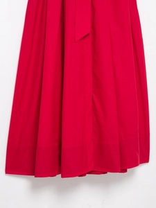 Close-up of vibrant red pleated cotton skirt featuring tie-waist detail and dense texture