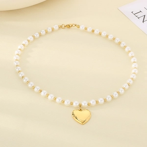 Detailed view of white pearls and golden heart pendant on a minimalist stainless necklace