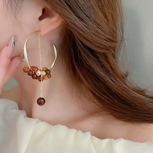 Close-up of dangling C-shape earrings with sandalwood beads and gold chains on a model