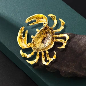 Golden alloy crab brooch with rhinestone details and needle clasp on dark rock background
