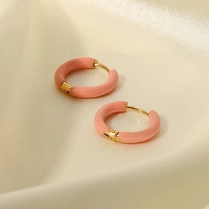 Primer plano de aros de esmalte rosa con base de metal dorado sobre tela de seda