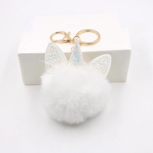 Close-up of white plush unicorn pom-pom keychain with glittery horn and gold hardware