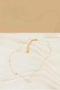 Detailed view of 18K gold pearl necklace with small white pearls on light silk background