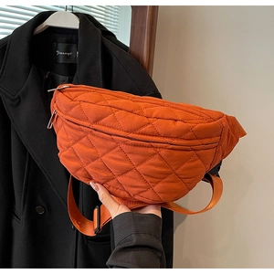 Detail of an orange quilted nylon crossbody bag featuring an adjustable strap on a model