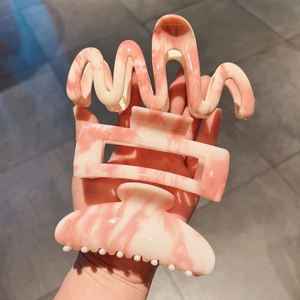 Close-up of three pink marble acrylic hair claws in wavy, rectangular and round shapes